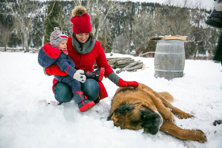A Woman and Child Sit With Dog in Snow at a Pet-Friendly Ranch.