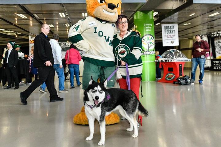 A Woman and Her Dog Poses With a Mascot at a Dog-Friendly Hockey Game in Iowa.