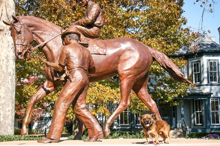 A dog sits next to a statue of Secretariat the racehorse.
