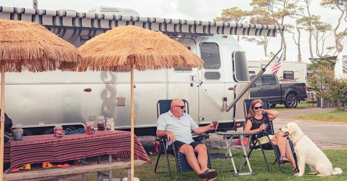 A couple and their dog sit outside an RV at a dog-friendly campground.