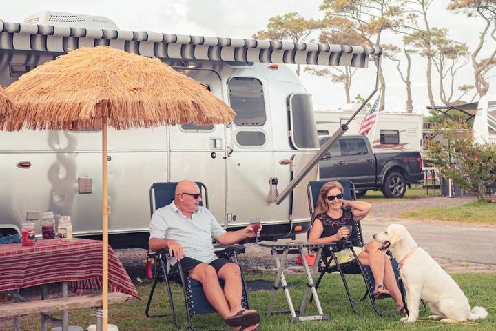 A couple and their dog sit outside an RV at a dog-friendly campground.