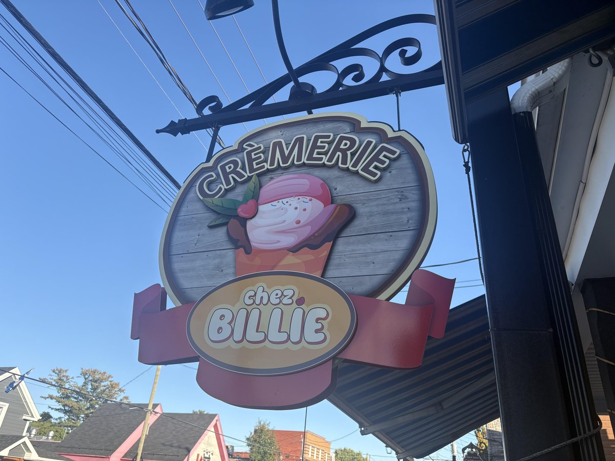 Round wooden sign with pink ice cream illustration hangs above entrance at dog-friendly Crèmerie chez Billie in Rawdon, QC.