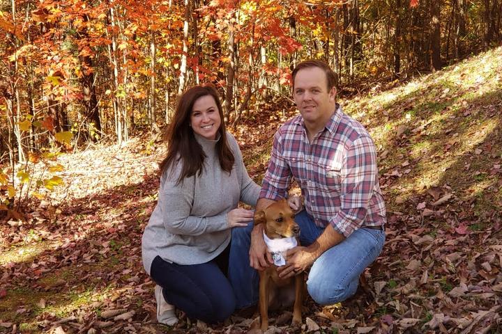 Dog sits with family in fall leaves.